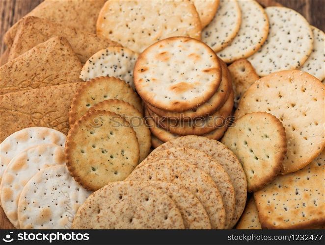 Various organic crispy wheat, rye and corn flatbread crackers with sesame and salt in round plate on wood background.