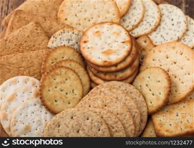 Various organic crispy wheat, rye and corn flatbread crackers with sesame and salt in round plate on wood background.