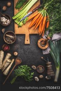 Various organic farm vegetables ingredients on dark rustic table with kitchen utensils, herbs and spices, top view. Frame. Copy space. Vegan and vegetarian food concept. Healthy cooking lifestyle