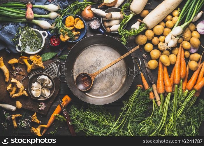 Various organic vegetables ingredients around empty aged cooking pot with wooden spoon on old kitchen table, top view