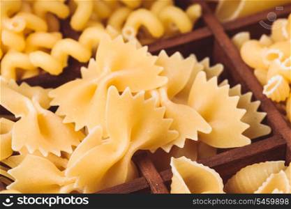 Various pasta types in the wooden box on the table. Close up farfalle