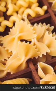 Various pasta types in the wooden box on the table. Close up farfalle