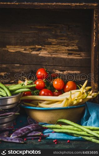 Various pea and beans pods with tomatoes on rustic wooden background