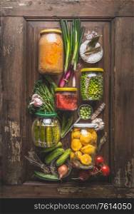 Various preserved vegetables in jars on rustic wooden background with ingredients, top view. Flat lay. Composition of canned food. Vegan. Home cuisine. Harvesting storage. Zero waste housekeeping