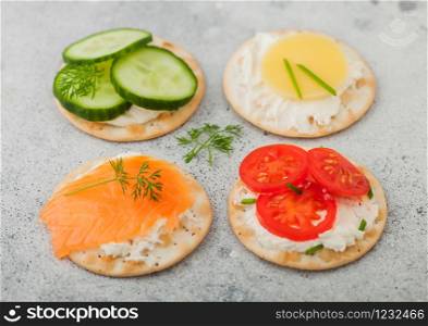 Various round healthy crackers with salmon and cheese, tomato and cucumber on light kitchen table background.
