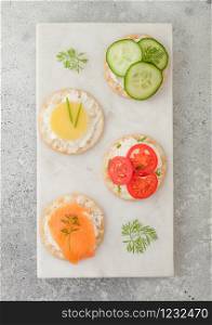 Various round healthy crackers with salmon and cheese, tomato and cucumber on marble board on light table background. Top view
