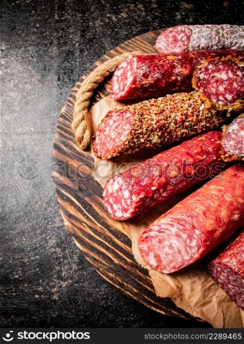 Various salami sausage on a wooden tray. On a black background. High quality photo. Various salami sausage on a wooden tray.