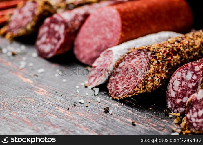 Various salami sausage on the table in a row. Against a dark background. High quality photo. Various salami sausage on the table in a row.