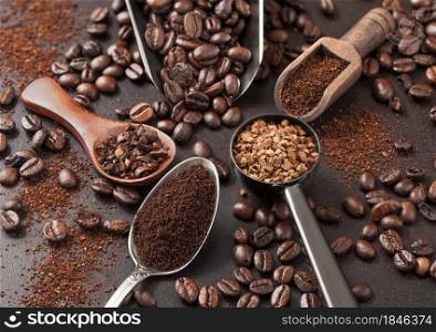 Various scoops with ground and bean coffee and freeze dried instant coffee granules on brown background. Macro