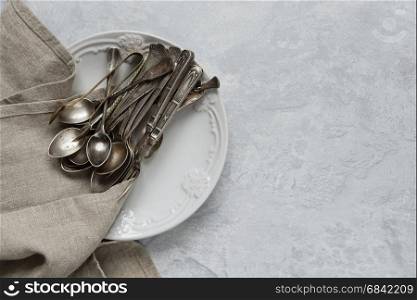 Various silverware on a ceramic plate on the background of gray concrete surface, with copy-space