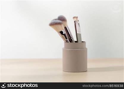 Various sizes of Rouge Brushes in pastel pink cup on a wooden table.