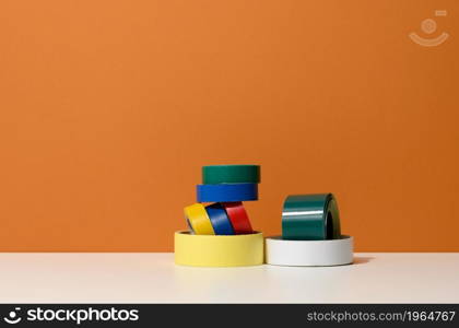 various skeins of multicolored scotch tape and electrical tape onorange background, copy space