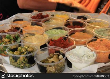 Various Spanish tapas in small plastic containers on a market stall, Olives, garlic sauce and various tapenades