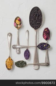 Various spoons with black and green tea, rose buds mix and blue mallow flowers and petals on white background. Top view