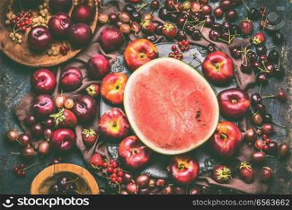 Various summer berries and fruits: watermelon, strawberries, peaches, plums, cherries, gooseberries, currants  on rustic kitchen table with flowers and plates, top view, flat lay. Organic local  food
