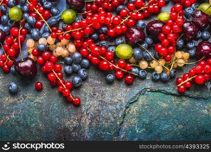 Various summer berries: gooseberries , red and white currants , cherries , blueberries on dark rustic background, top view, border