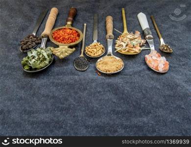 Various teas and dried herbs assortment on spoons in rustic style on balck background. Organic herbal. Selective focus.