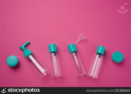 Various transparent empty plastic bottles and jars for cosmetics on a pink background, top view