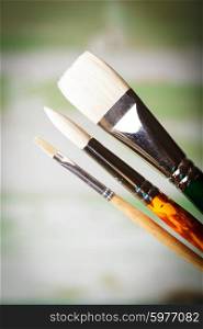Various types of paint brushes over the defocused painting. Paint brushes