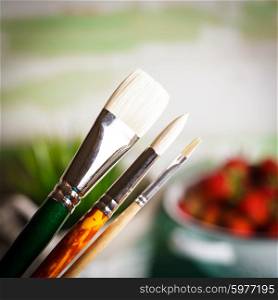 Various types of paint brushes over the defocused painting. Paint brushes