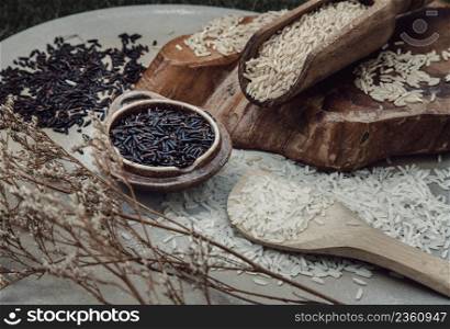 Various types of rice : Brown rice, Jasmine rice, Riceberry and dried flowers on ceramic background. Organic raw rice collection, Healthy food and diet concept, Overhead view, Selective focus.