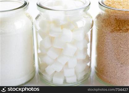 Various types of sugar in a glass jar on white background.