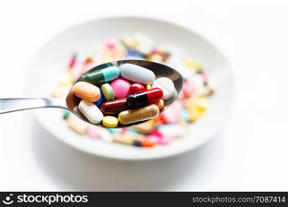 Various types of tablets, capsules and pills on spoon with colorful medicine background. Top view