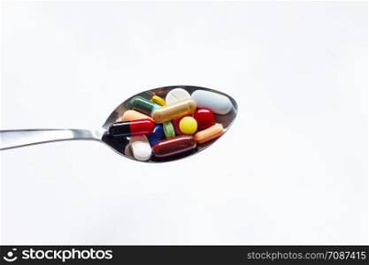 Various types of tablets, capsules and pills on spoon with white background
