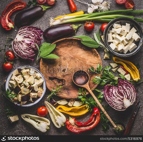 Various vegetables cooking ingredients around wooden plate with spoon on rustic background with bowls. Vegetarian cooking preparation for tasty dishes, top view. Healthy eating concept