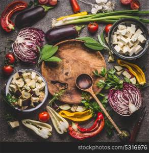 Various vegetables cooking ingredients around wooden plate with spoon on rustic background with bowls. Vegetarian cooking preparation for tasty dishes, top view. Healthy eating concept