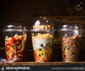 Various vegetarian salads in plastic cups on dark wooden background. Healthy Take away lunch