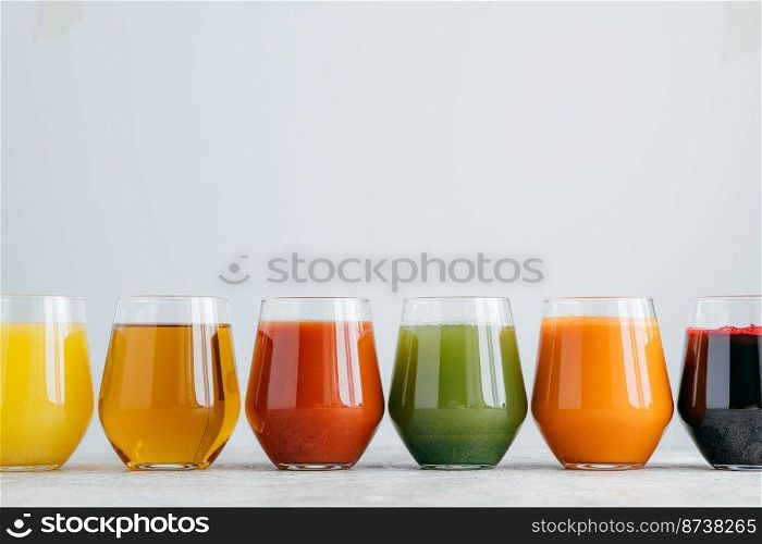 Vartiety of oranganic drink in glasses. Assorted multicolored juice in jar standing at row against white background, empty space above