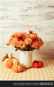 Vase with flowers and small orange textile pumpkins on a table. Autumn decor on table
