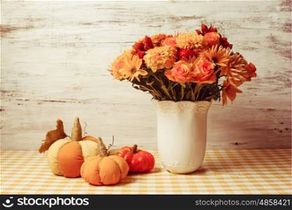Vase with flowers and small orange textile pumpkins on a table. Autumn decor on table