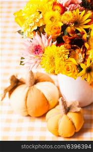 Vase with flowers and small orange textile pumpkins on a table. Autumn table decor
