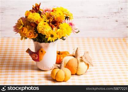 Vase with flowers and small orange textile pumpkins on a table. The Autumn decor