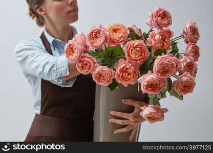 Vase with pink roses. A smiling woman holding a florist holds pink roses on a gray background. Business and floristry concept. Girl florist with a big bouquet of pink roses around a gray background. The concept of a flower shop