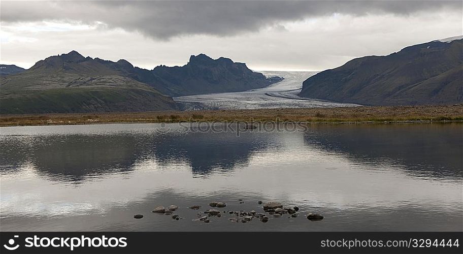 Vatnajokull glacier, mountains, and clouds reflected in water along coastline