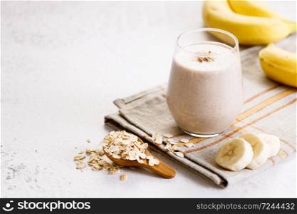 Vegan banana and oatmeal smoothie in a glass on white marble background. Healthy food concept.