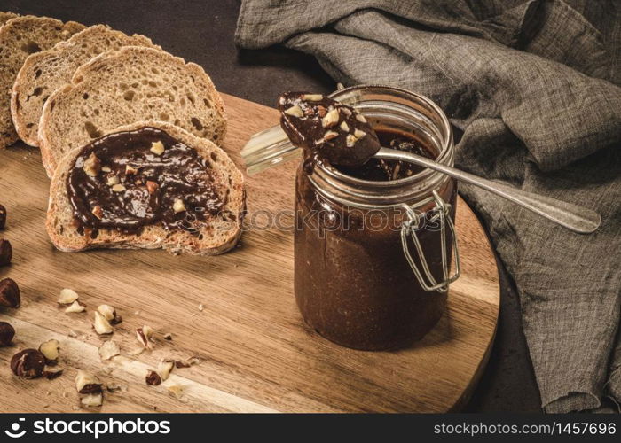 Vegan chocolate spread made of organic almond butter and organic cacao and honey, on dark rustic kitchen counter top.