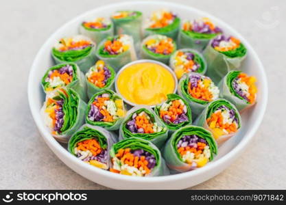 Vegan food concept. Tasty green spring rolls made of rice paper and spinach, filled with fresh chopped vegetables. Small plate with yellow curry sauce in middle