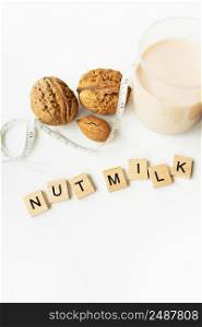 Vegan milk from nuts in a glass cup with various nuts on a white table. Lettering nut milk. Vegan milk from nuts in a glass cup with various nuts on a white table. Lettering nut milk.