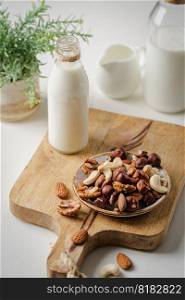 Vegan milk from nuts in glass jar with various nuts on white stone background. Vegan milk from nuts
