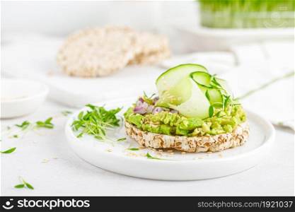 Vegan open sandwich with dietary crispbread, fresh cucumber, onion, sesame seed, microgreens and avocado. Healthy vegetarian food, diet.