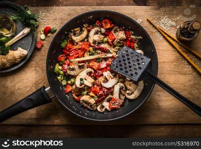 Vegan stir fry in pot on wooden background, top view. Chopped roasted vegetables in frying pan. Asian food and eating , Chinese or Thai cuisine concept