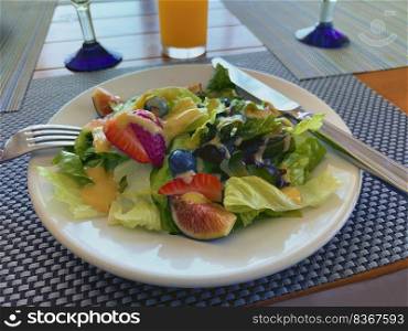 Vegetable and fruit salad with strawberry, fig, blueberry, lettuce with honey mustard dressing on top 