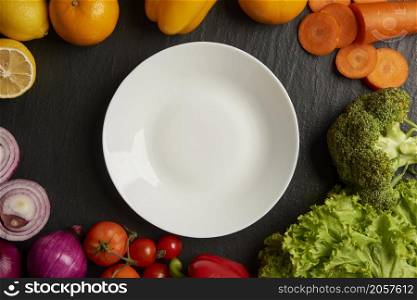 vegetable concept various types of vegetables being placed around a white plate on the black background.