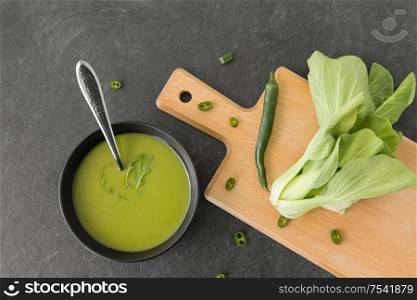vegetable, food and culinary concept - bok choy chinese cabbage cream soup in ceramic bowl with spoon on slate stone background. bok choy chinese cabbage cream soup in bowl