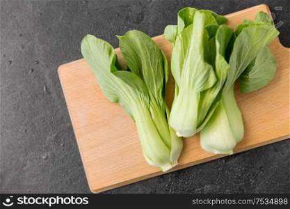 vegetable, food and culinary concept - close up of bok choy chinese cabbage on wooden cutting board on slate stone background. bok choy chinese cabbage on wooden cutting board
