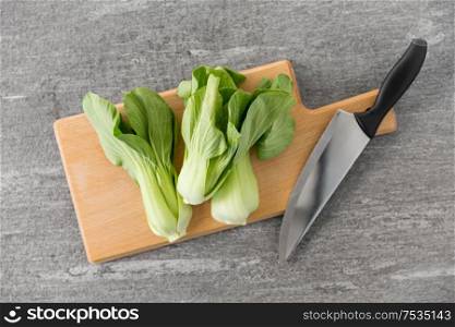 vegetable, food and culinary concept - close up of bok choy chinese cabbage and kitchen knife on wooden cutting board on slate stone background. bok choy cabbage and knife on cutting board